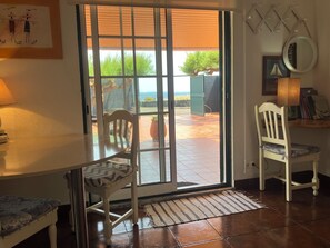 Una habitación con puerta de cristal corredera que da a un patio exterior, una mesa de madera, una silla, una alfombra pequeña y una lámpara fijada a la pared.