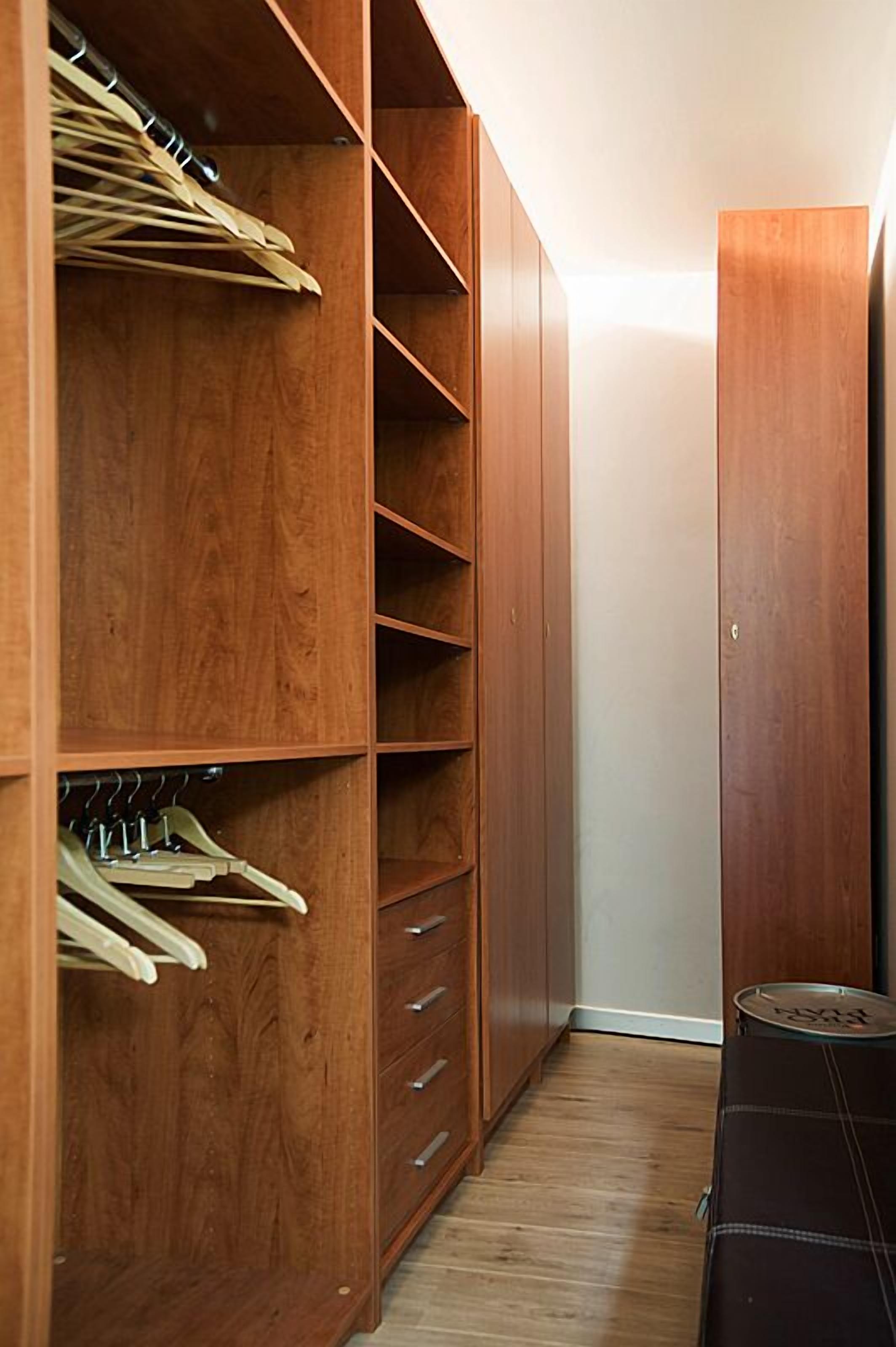 Un placard en bois avec plusieurs étagères et un espace pour suspendre des vêtements, une petite table et une valise.