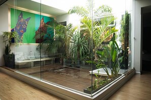 Ein modernes Wohnzimmer mit Glastrennwand, einer Couch und verschiedenen Zimmerpflanzen.
