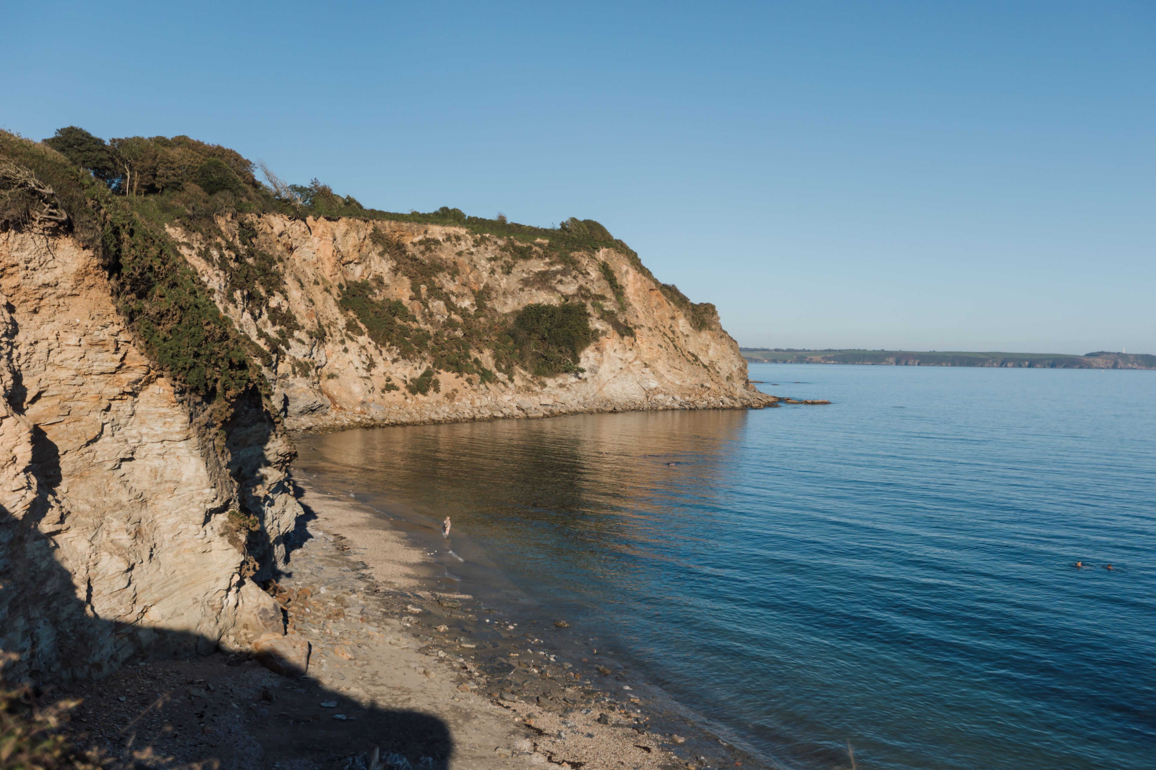 A coastal landscape with a rocky cliff and calm sea.