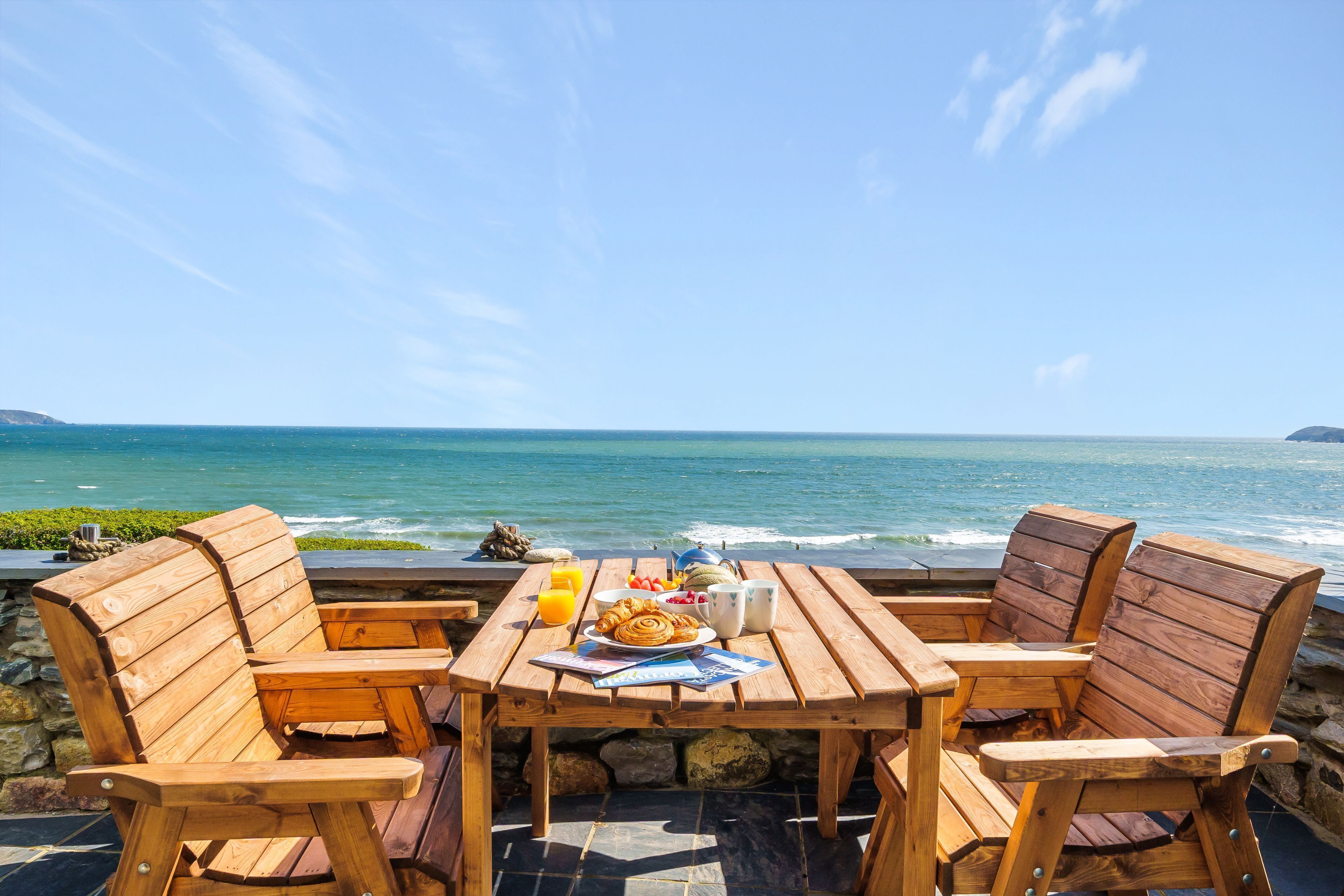 A wooden table and chairs with a view of the ocean.