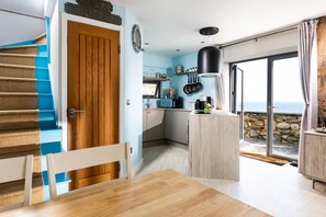 Eine moderne Küche mit Holztür, ein Essbereich mit Tisch und Meerblick durch eine Glastür.
