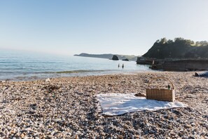 Une plage de galets avec un coin pique-nique comprenant un panier et une couverture.