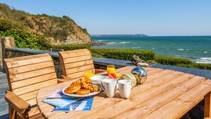 A wooden table with breakfast items, a magazine, and a view of the ocean. - As seen on TV! Luxurious Beach Front Cottage with Hot Tub, Log Burner & Sea Views (Charlestown)
