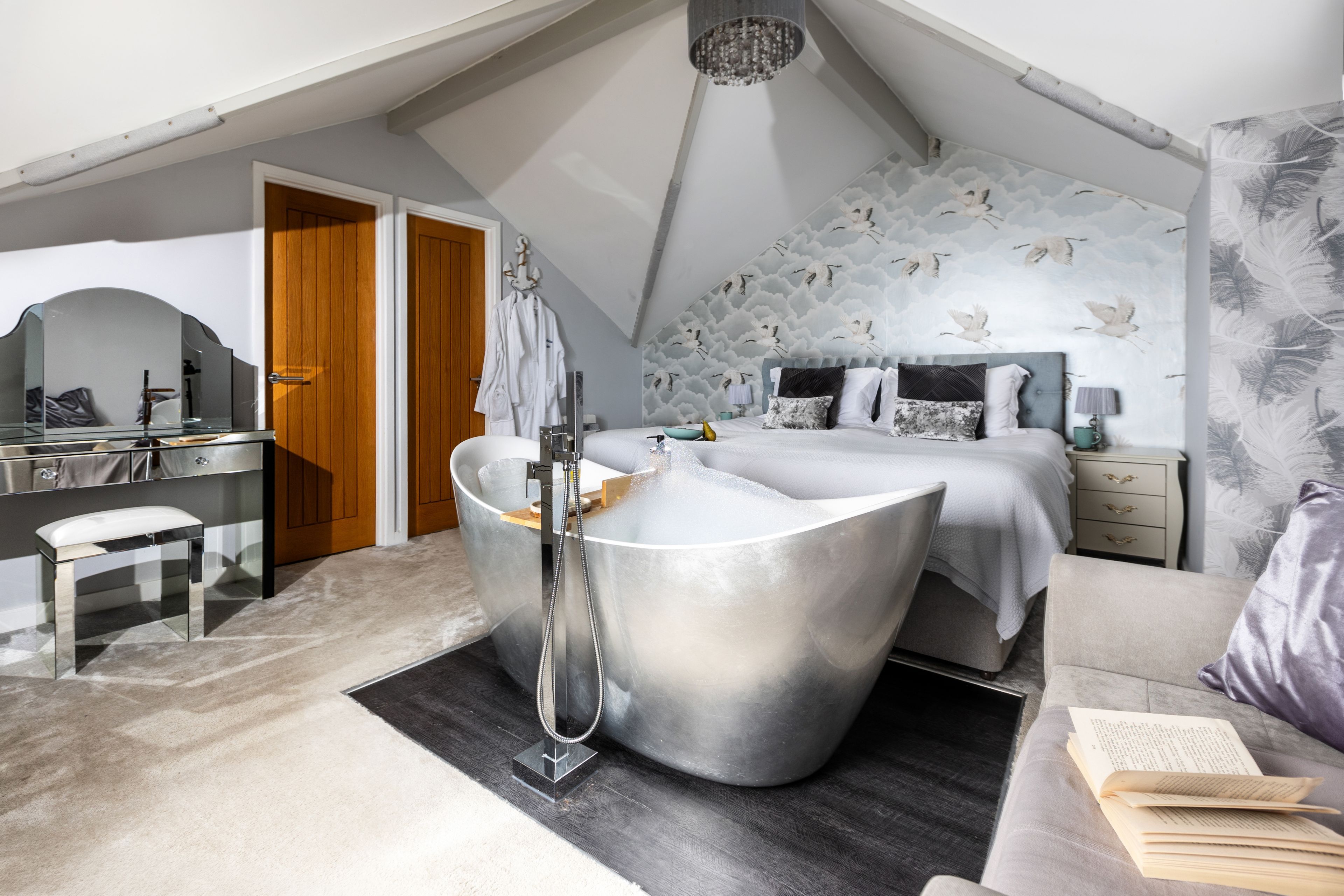 A modern bedroom with a large bathtub, a desk, and a bed with a patterned headboard.