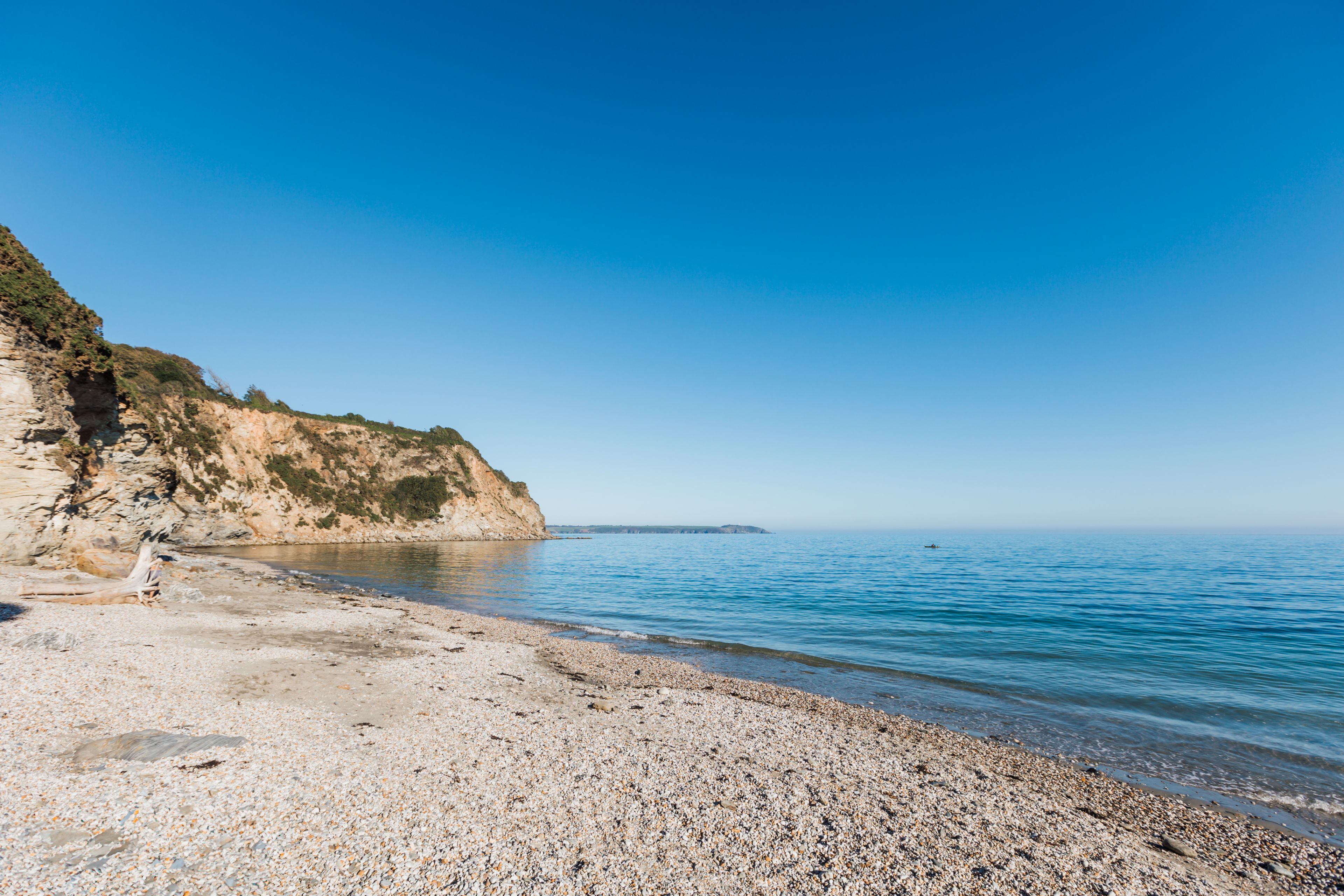 Una playa de guijarros con vista despejada al mar y un acantilado rocoso.