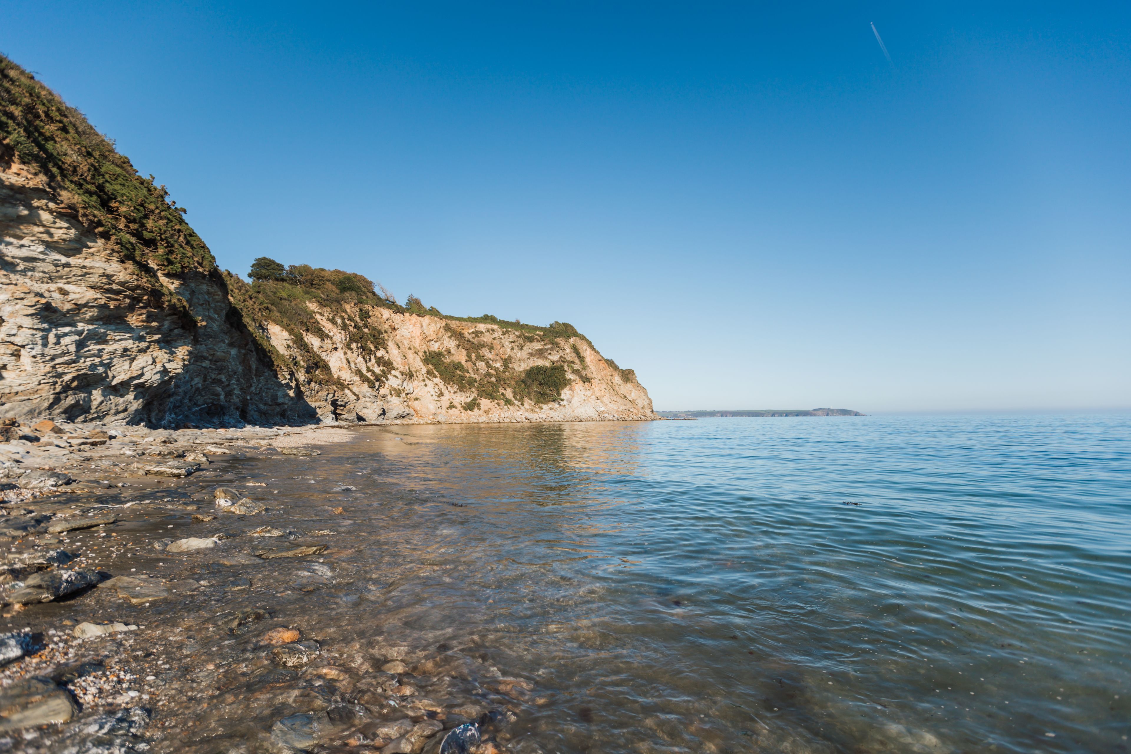 Un paisaje costero con aguas cristalinas, costa rocosa y un acantilado escarpado.