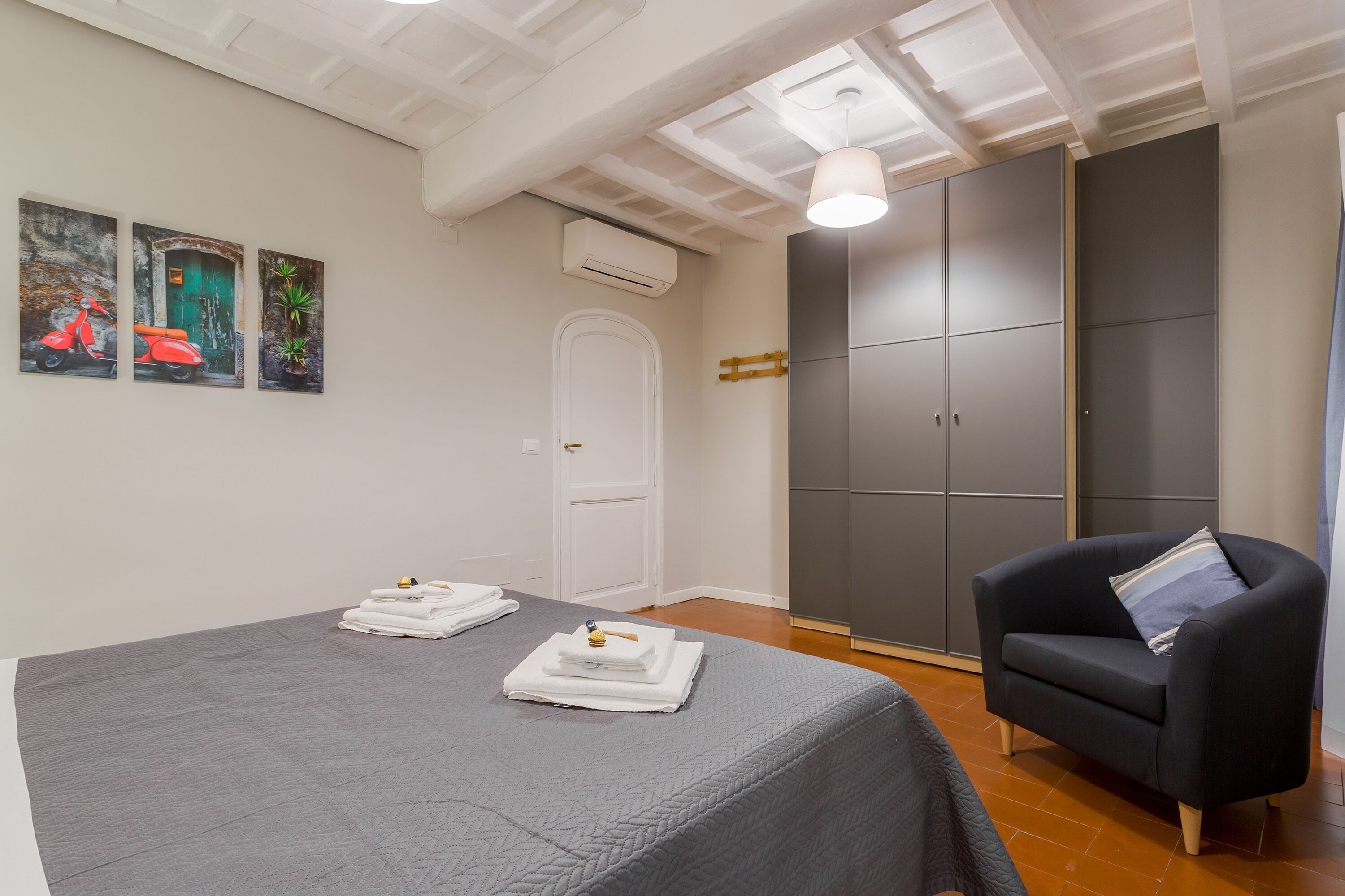 A bedroom with a bed, a chair, a wardrobe, and artwork on the wall.
