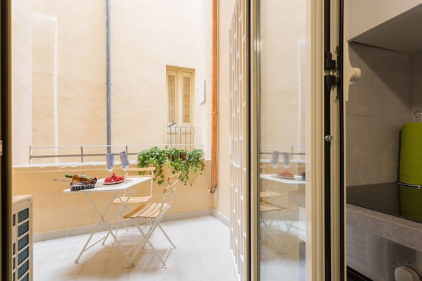 A compact balcony with a table, chairs, a grill, and a potted plant.