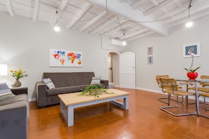 A modern living room with a grey sofa, a wooden coffee table, and a dining area with a table and chairs.