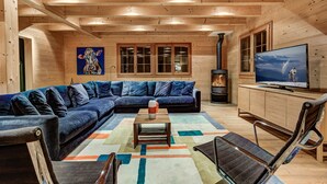 Un intérieur chaleureux de chalet en bois, avec un canapé d’angle, un téléviseur à écran plat et une cheminée.
