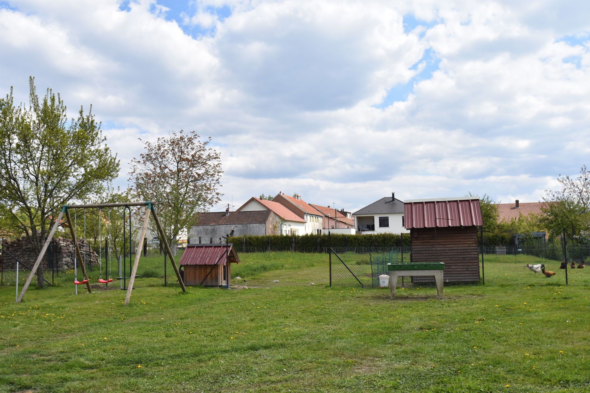 Ein grünes Rasenstück mit Schaukel, einer kleinen Gartenhütte und einem umzäunten Bereich mit Hühnern.