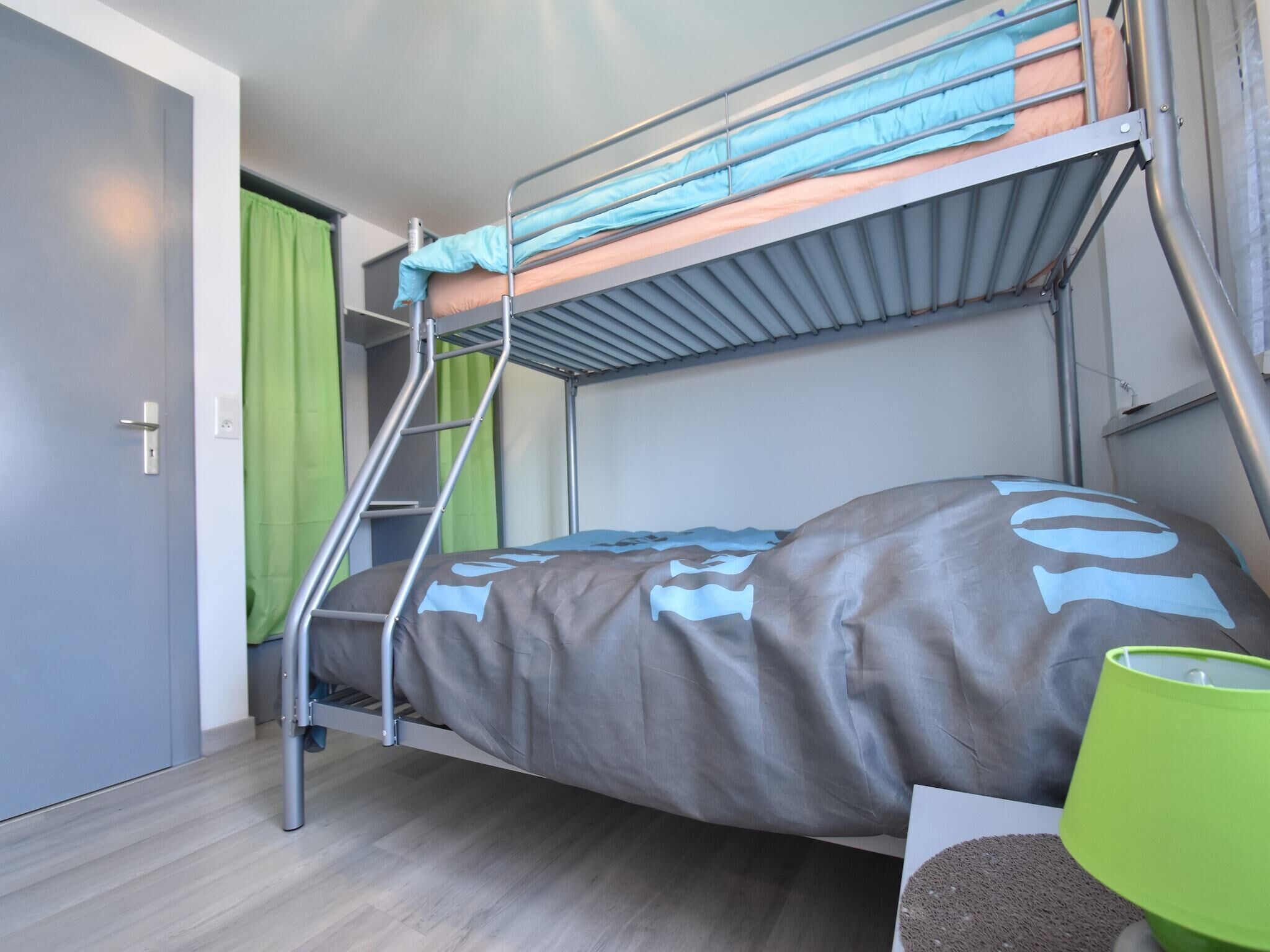 A bunk bed with a ladder, a green curtain, and a green lamp on a wooden floor.