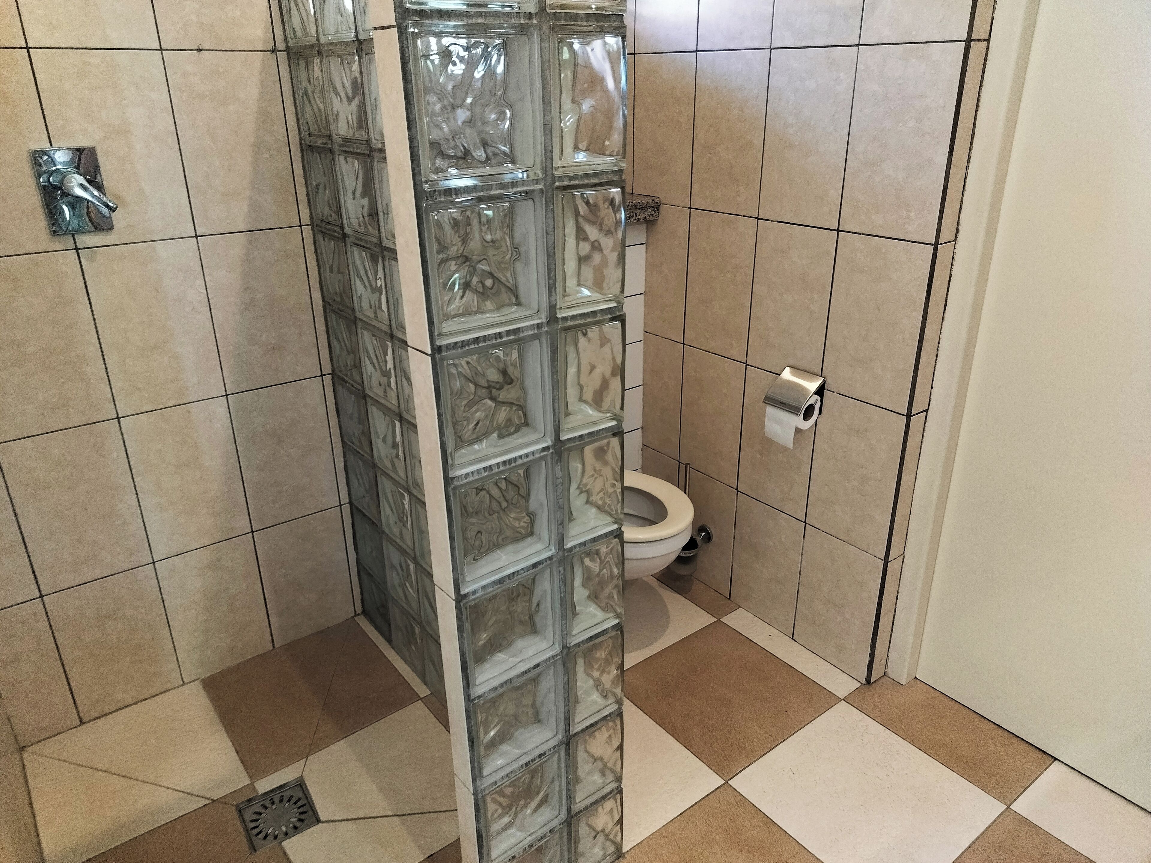 A bathroom with a glass shower enclosure, a toilet, and a paper towel dispenser.