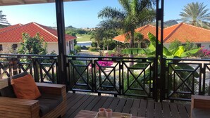 En træterrasse med sofa og bord, med udsigt over et smukt landskab med huse med røde tage og palmer.