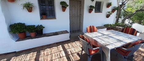 An outdoor patio with a table and chairs, surrounded by potted plants and a wooden door.
