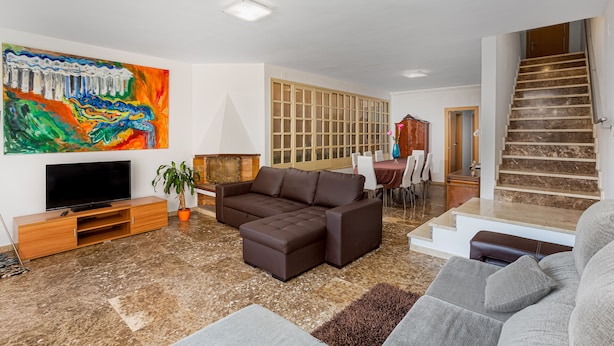 Un salon moderne avec un canapé d’angle, un téléviseur à écran plat et un tableau abstrait aux couleurs vives.