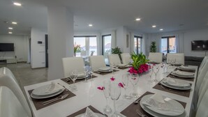 Een eethoek met een lange tafel gedekt voor een maaltijd, witte stoelen en uitzicht op zee door grote ramen.
