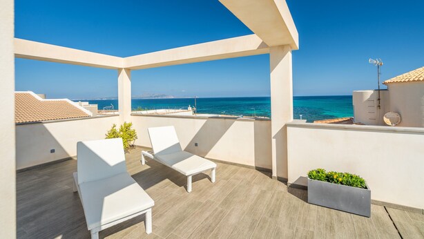 Een balkon met witte lounge stoelen, een kleine plantenbak en uitzicht op zee.