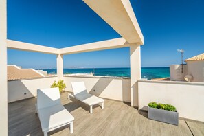 Een balkon met witte lounge stoelen, een kleine plantenbak en uitzicht op zee.