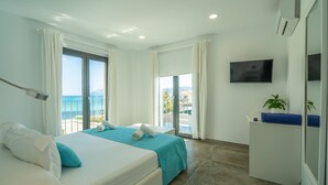 Een hotelkamer met een bed, een televisie, een bureau en uitzicht op zee.
