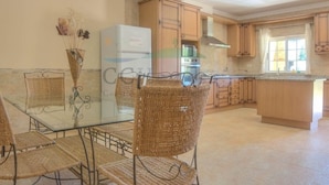 A kitchen with a glass dining table, wicker chairs, wooden cabinets, and a built-in oven. - wonderful villa with beautiful view of the mountains  (Estoi)