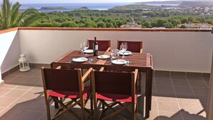 Et spisebord på en terrasse med havudsigt og grønne omgivelser.