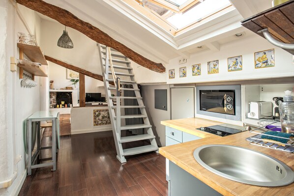 A modern kitchen with a wooden staircase, a built-in oven, and a large window above the sink.