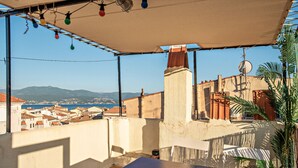 Terraço com mesa e cadeiras, vista para uma cidade costeira e montanhas.
