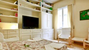 Una habitación de hotel con una cama, televisión, estantería y una silla.