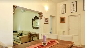 Un comedor con una mesa de madera, un florero con una vela morada y un corredor rojo. Se observa una puerta blanca y un cuadro en la pared.