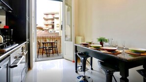 Una cocina moderna con comedor, una puerta corrediza de vidrio que da a un balcón y vista a un edificio de enfrente.