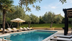 A swimming pool with lounge chairs and umbrellas, surrounded by greenery.