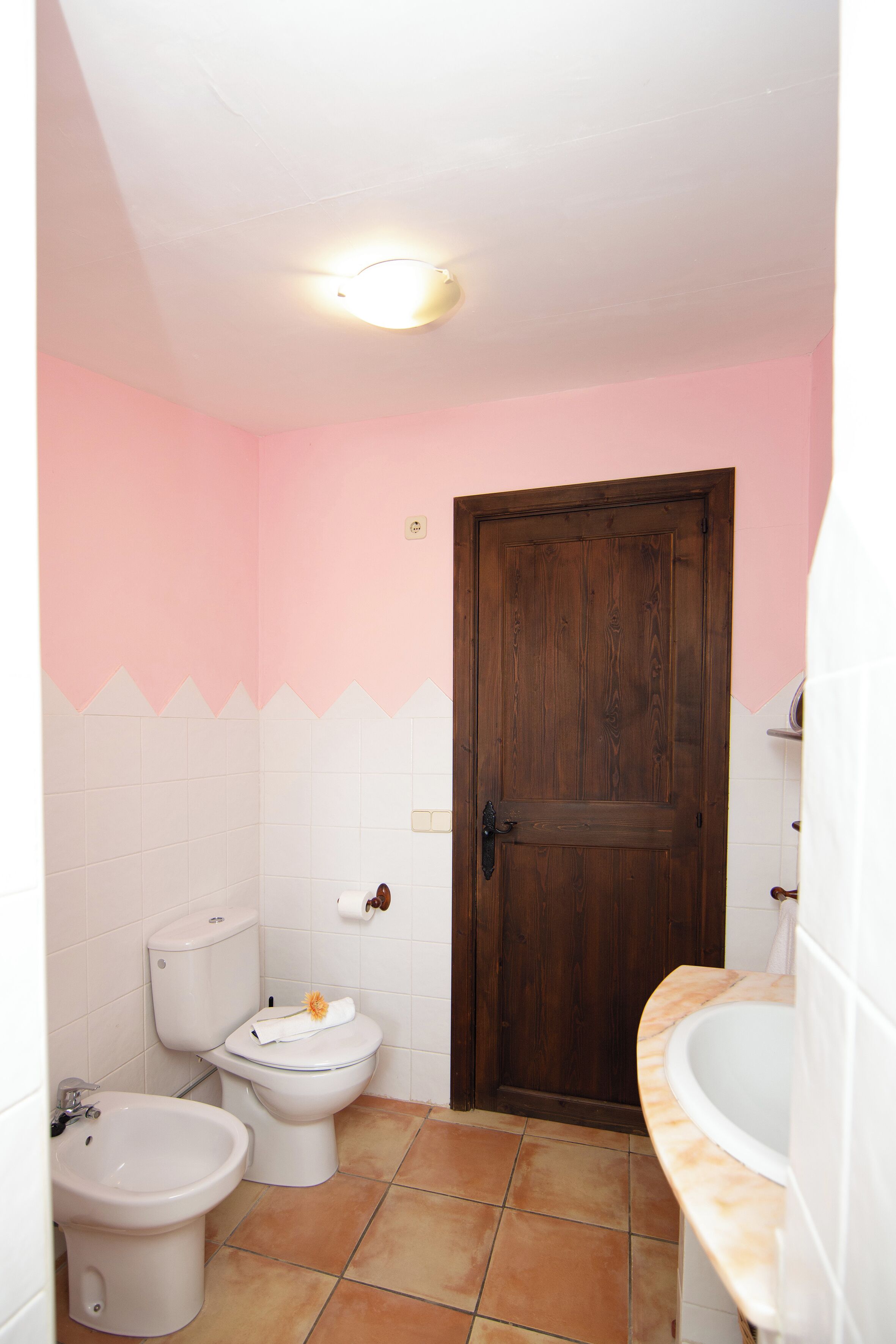 Une salle de bain avec une porte en bois, des toilettes blanches, un bidet et un lavabo.