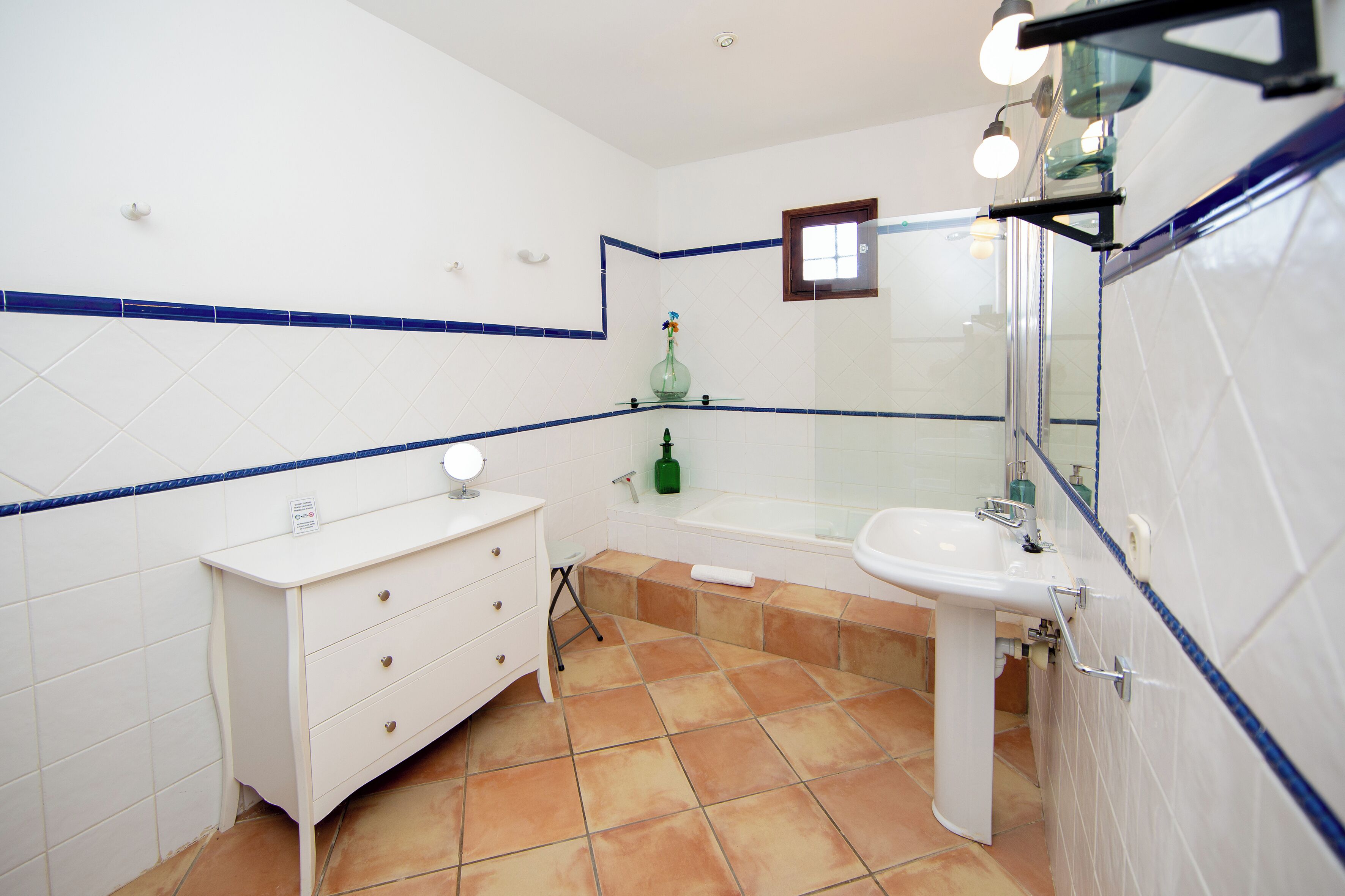 A bathroom with a white sink, a mirror, a green bottle, and a white cabinet.