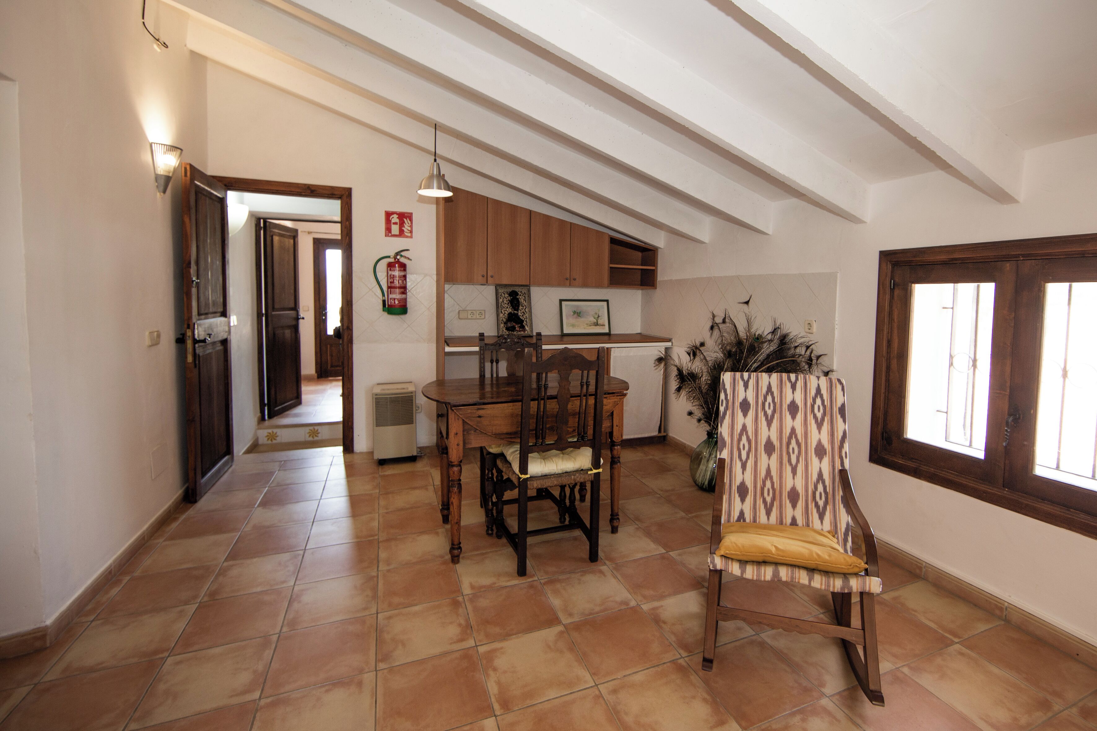 Un'ampia zona pranzo con tavolo e sedie in legno, pavimento piastrellato e vista sulla cucina sullo sfondo.