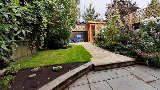 A garden with a paved pathway, a wooden fence, and a small outdoor seating area.