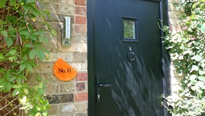 A dark green door with a small window, a doorbell, and a mailbox on a brick wall.