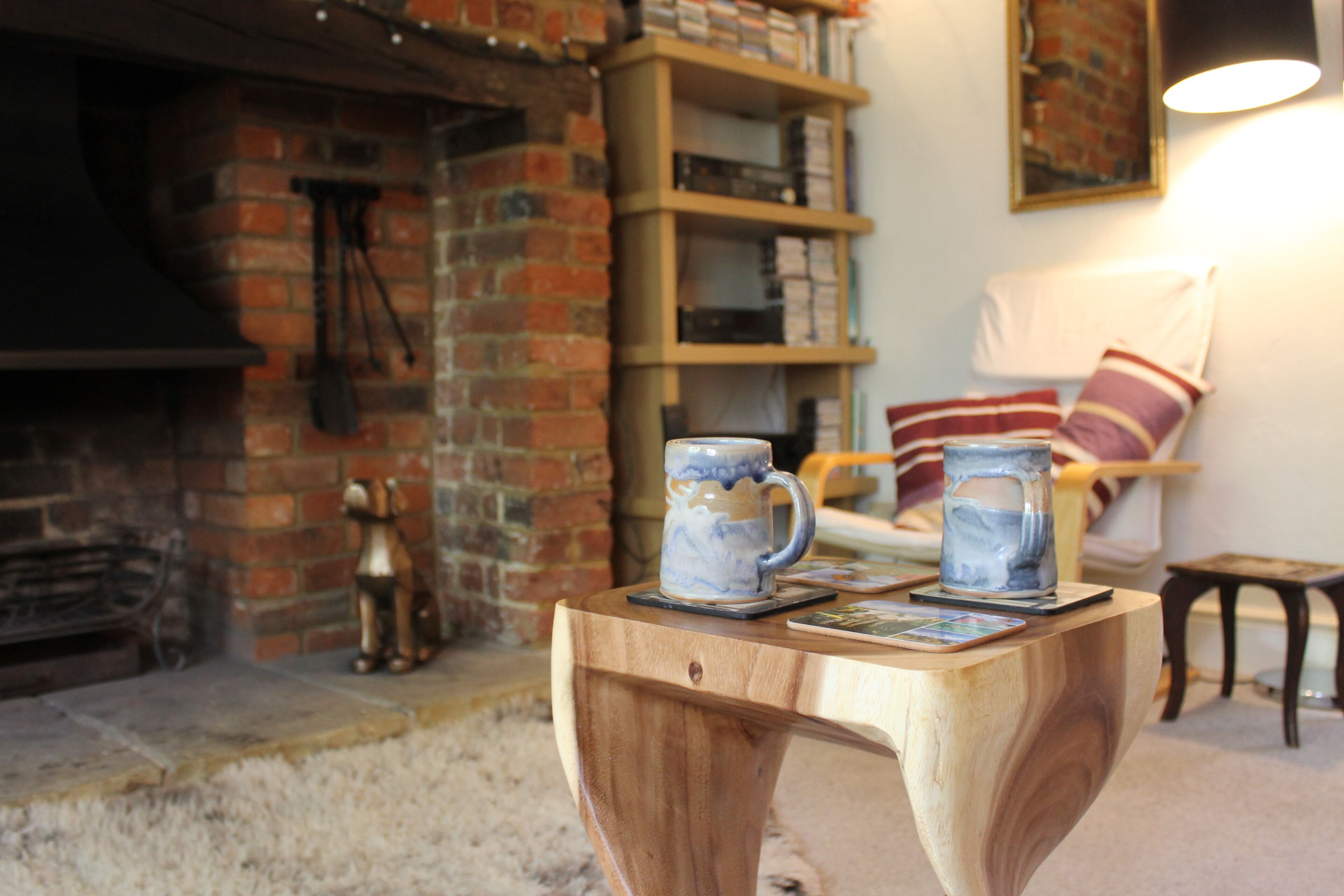 A cozy living room with a fireplace, a wooden coffee table with two mugs, and a bookshelf in the background.