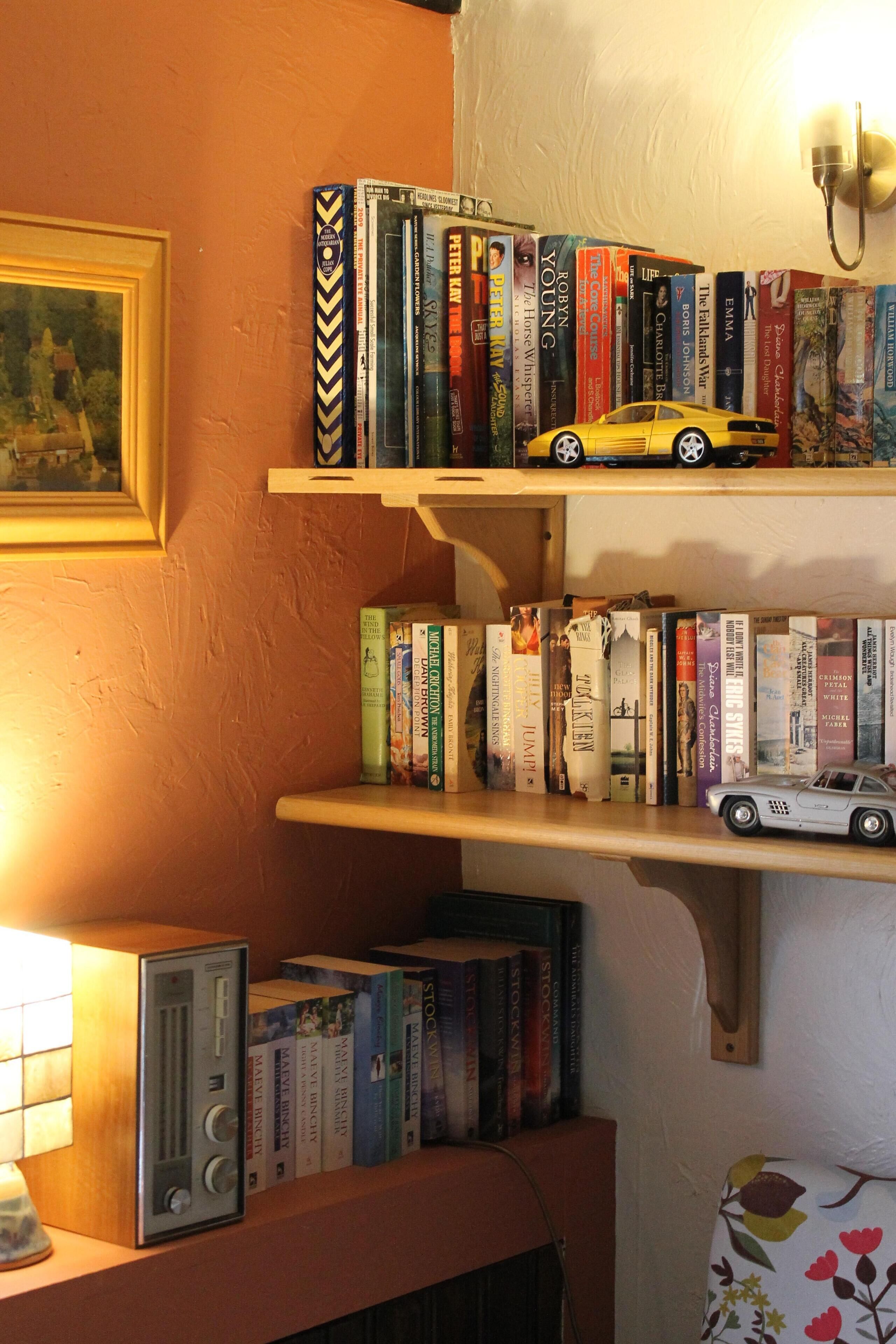 Une bibliothèque avec des livres et deux voitures jouets, un tableau encadré et une radio posée sur une étagère.