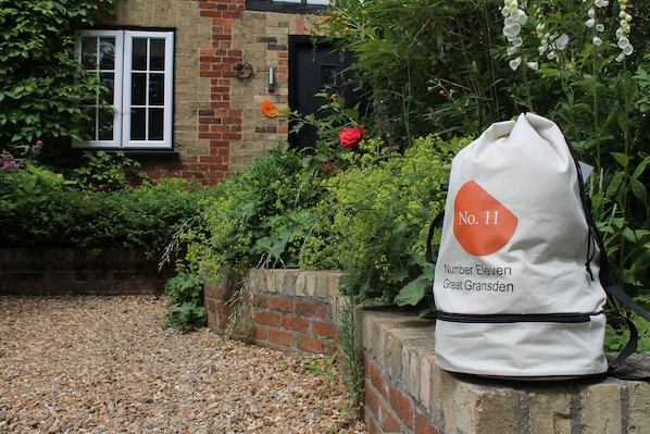 A white bag with "No. 11" and "Number Eleven Great Gransden" text, placed on a brick ledge near a brick building with a window and greenery.