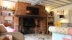 A cozy living room with a brick fireplace, a flat-screen TV mounted above it, and a bookshelf filled with books.