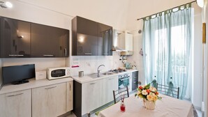 Cocina moderna con televisor de pantalla plana, microondas, fregadero y estufa. Cuenta con un comedor con mesa y sillas, además de una ventana con cortinas.