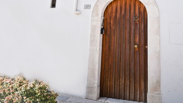 Un edificio blanco con puerta de madera y dos ventanas con barandillas blancas.