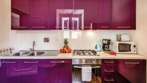 A kitchen with purple cabinets, a stainless steel sink, a gas stove, a microwave, and a toaster.
