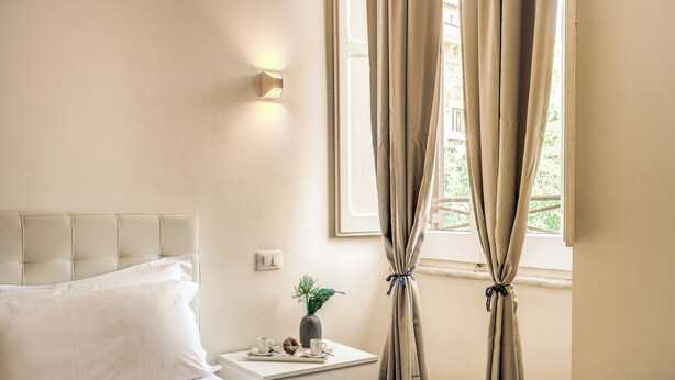 A neatly arranged bedroom with a bed, bedside table, and curtains.
