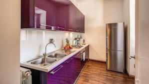 A modern kitchen with stainless steel appliances, purple cabinets, and a wooden floor.