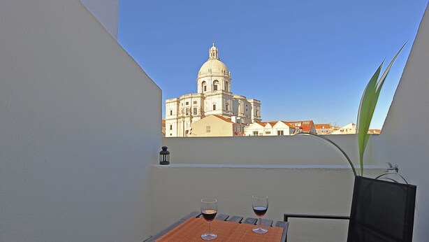Ein Balkon mit Tisch und zwei Gläsern Rotwein, mit Blick auf ein historisches Gebäude mit einer Kuppel.