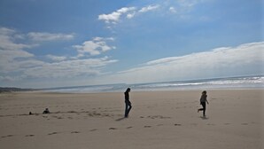 Ein weiter, sandiger Strand mit Fußabdrücken und zwei Personen, die spazieren gehen.