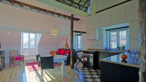 Ein großzügiger Loft mit hoher Decke, freiliegenden Holzbalken, einem Essbereich mit Schachbrettmuster und einer Küche mit schwarzer Arbeitsplatte, sowie großen Fenstern, die für natürliches Licht sorgen.